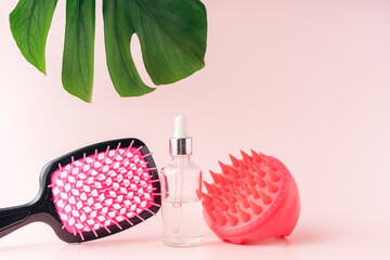 Scalp massager with oil and comb against pink background.