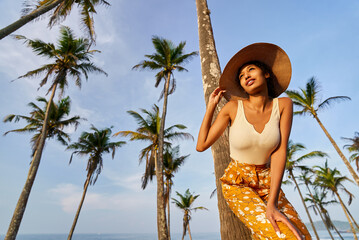 Young african female model posing in colorful clothes at tropical location at sunrise. Black woman against exotic scenery at dawn. Multiracial dark-skinned model poses in front of palm trees at sunset