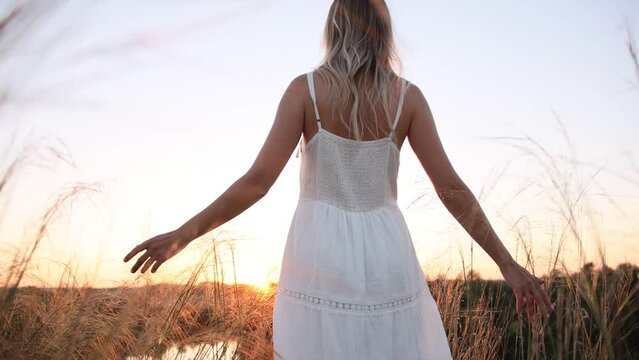 Young pretty woman in dress walks outdoors in field with amazing sunset. slow motion