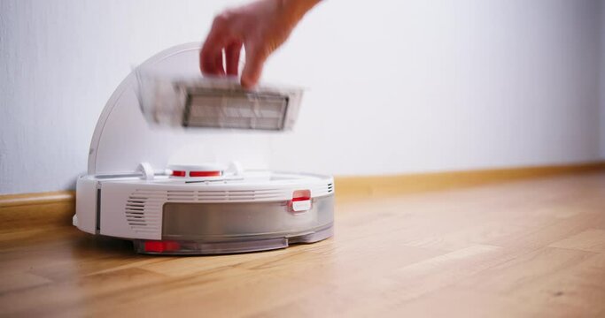 container with dust from vacuum cleaner robot. Close up of man doing maintenance on robot cleaner at home.