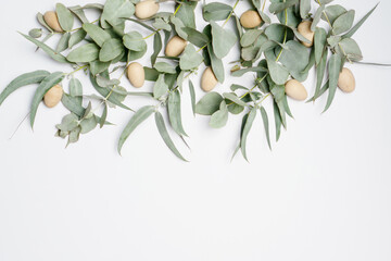 Beautiful flat lay easter composition of wooden easter eggs and eucalyptus leaves on a white background, with space for copy.