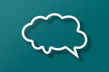 White paper cut out speech bubble shape set on green paper background.