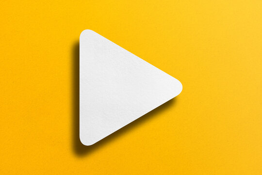 White paper cut into triangle shape, play button set on yellow paper background.