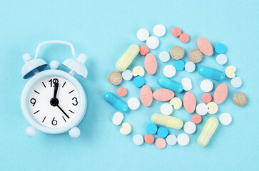 Fototapeta na wymiar Medicine time. High angle view of colorful medicines and pills on alarm clock.