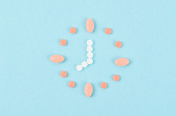 The Clock created from pink and white pills on blue background. Right time for using medicines.