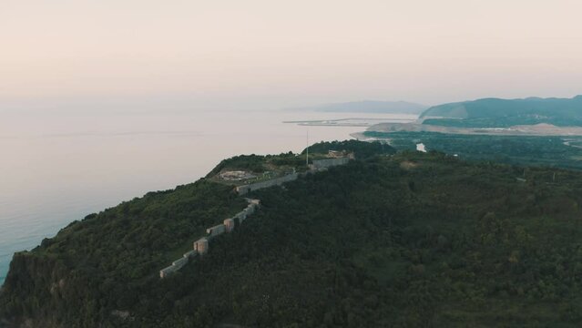 Drone view of the lighthouse in the trees, the white lighthouse building built on the edge of the cliff