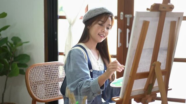 Young female painter mix color on palette to painting artwork on canvas with enjoy in home studio
