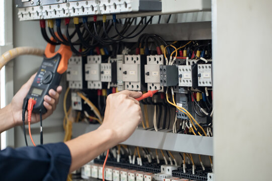 Electrician engineer work tester measuring voltage and current of power electric line in electrical cabinet control , concept check the operation of the electrical system .