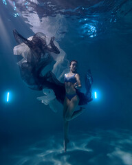 a young beautiful girl is swimming in a pool under water fashion fabric on a dark blue background...