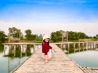 Fototapeta premium Young girl enjoying beauty of nature looking at lake. Adventure travel of woman sits on wooden bridge.