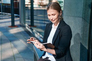 Business woman in suit is in city center against backdrop building, writes, writes down, takes notes, keeps a pen and notebook, brainstorms, creates ideas.