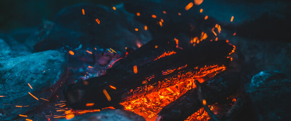 Fototapeta na wymiar Vivid smoldered firewoods burned in fire closeup. Atmospheric background with orange flame of campfire. Wonderful full frame image of bonfire with glowing embers in air. Warm logs, bright sparks bokeh