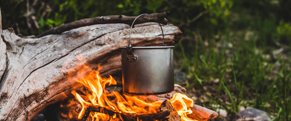 Kettle hanging over fire. Cooking food at fire in wild. Beautiful big log burns in bonfire...