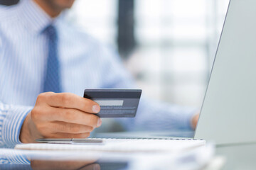 Smiling man sitting in office and pays by credit card with his laptop.