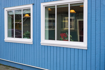 Two windows with white wood frames in a blue color wooden wall. Exterior of a wooden house with windows