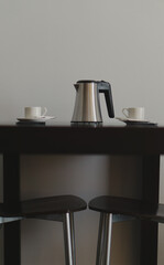 two white cups and a coffee pot on a black wooden table and two chairs