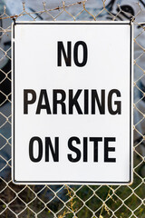 A black and white No Parking sign is attached to a wire fence in front of a building site