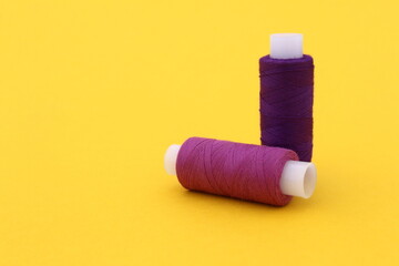  On a yellow background are two spools of purple thread.
