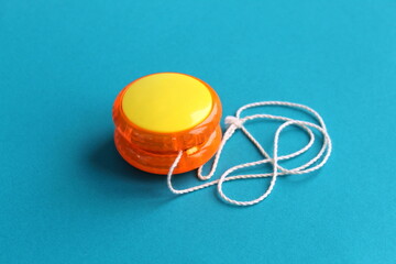 A plastic yo-yo toy of orange color with a thread lies on a turquoise background.