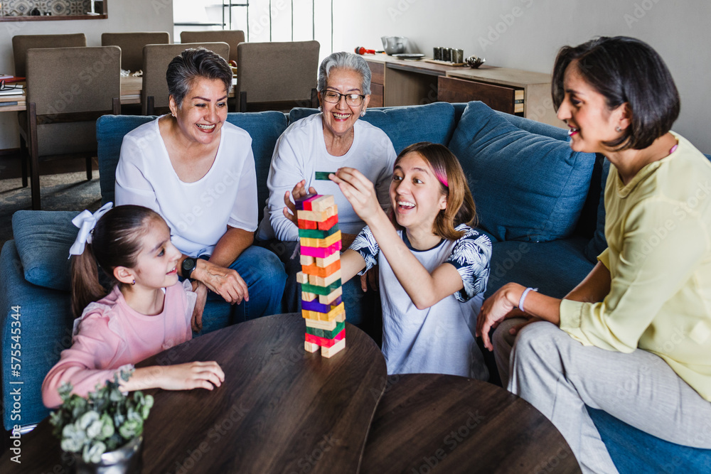 Wall mural hispanic family playing jenga game with grandmother and daughter at home, three generations of women