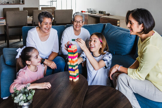 Hispanic Family Playing Jenga Game With Grandmother And Daughter At Home, Three Generations Of Women In Mexico Latin America