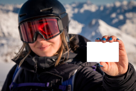 Front view, portrait of happy smiling woman skier showing map, ski pass, pass on slope with snowy mountain in background