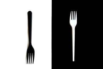  A white fork lies on a black background and a black fork lies on a white background.