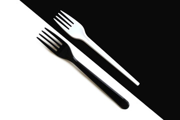 A white fork lies on a black background and a black fork lies on a white background.