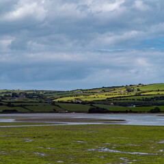 Open seabed after low tide, swamp area. Green hilly landscape. White clouds, sky. The coast of County Cork. Irish European landscape