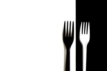 A white fork lies on a black background and a black fork lies on a white background.