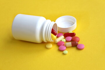 On a yellow background are medicine pills poured out of a white container.