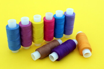 On a yellow background there are many bright multi-colored threads for sewing.