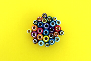 A bunch of bright thread spools for sewing lie on a yellow background, top view.