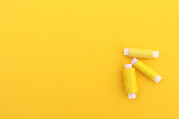 Several spools of yellow thread lie on a yellow background with space for text.