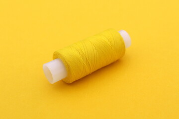 Fototapeta na wymiar On a yellow background lies one spool of yellow thread.