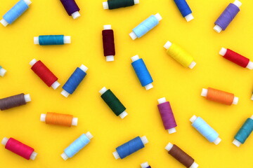 Many spools of multi-colored threads are scattered over a yellow background.