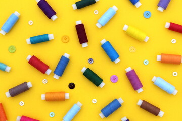 Many spools of multi-colored threads and buttons lie scattered on a yellow background.