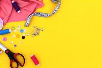 Sewing accessories lie on a yellow background, top view.