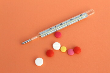 On an orange background lies a thermometer and medicine pills.