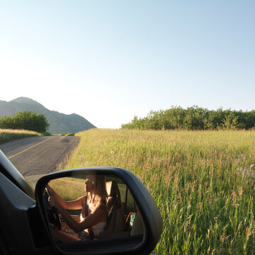 Detail of woman in side mirror of car in prairie meadow