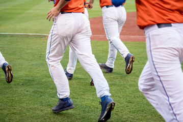 Leg only view of a group of baseball players running on the grass of a baseball field.