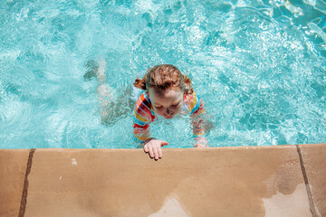 young girl holding on to side of pool