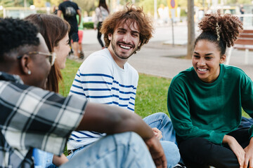 Young friends sitting on the grass, talking and sharing happy good times - focus on African...