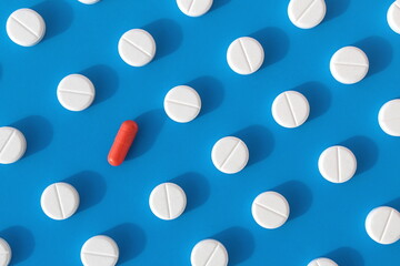 Abstract background of white pills on a blue background with one red capsule.