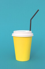 A bright disposable paper cup for coffee stands on a turquoise background.
