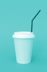 A bright disposable paper cup for coffee stands on a turquoise background.