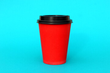 A bright disposable paper cup for coffee stands on a turquoise background.	