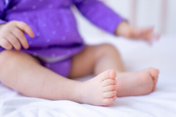 the legs or feet of a small newborn baby on a white cotton bed at home in a crib, pink baby heels