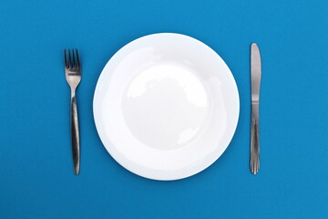 On a blue background is a plate with a fork and a knife.
