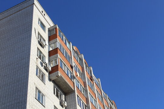 A high-rise multi-storey brick house stands against a blue sky, photo from bottom to top.